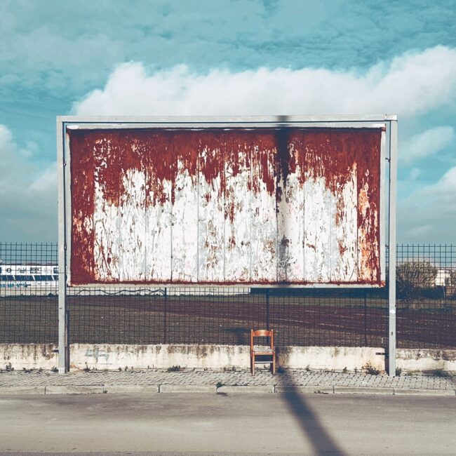 Persiinloro series by Sofia Dell'Aversano Orabona: a rusty empty billboard by the road under a blue sky